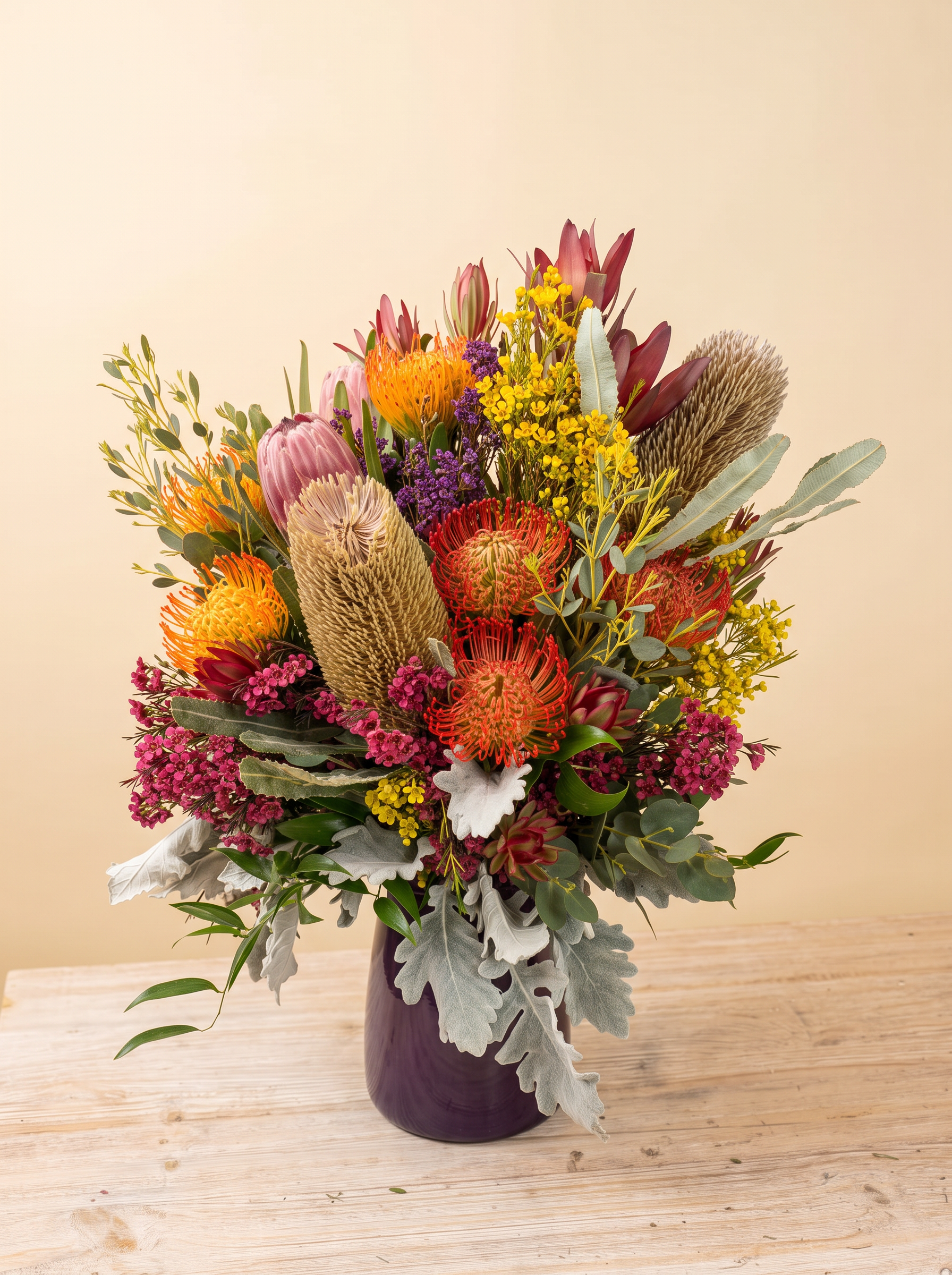 A Flowers by LD arrangement of protea, pincushions, banksia and wax flower in a purple vase